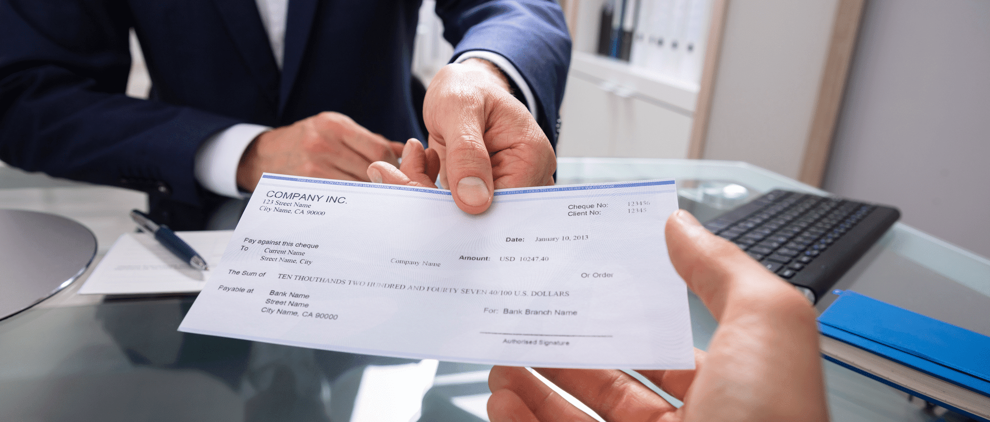 Businessman's-Hand-Giving-Cheque-Over-Glass-Desk